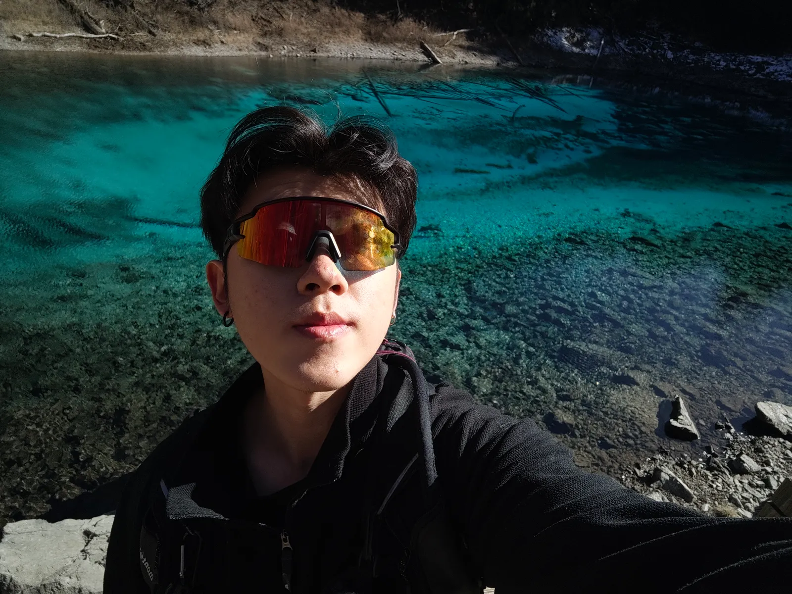 A selfie of Lin in mirrored sports sunglasses, in front of a clear turquoise lake.