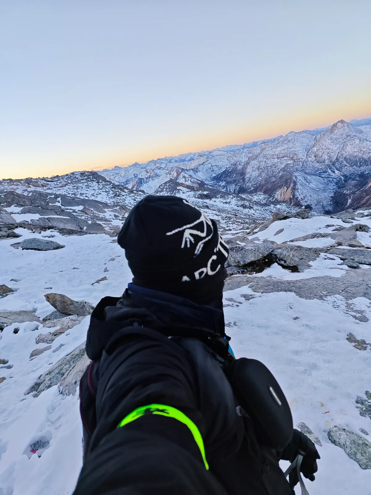 Lin from behind, in a beanie and a dark jacket, looking out over snow-covered mountains at first light.