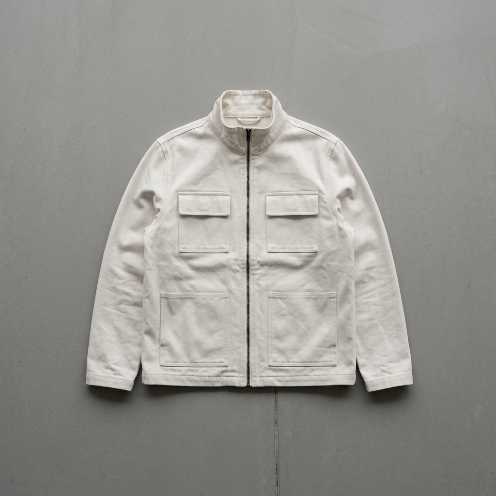 The bone canvas work jacket laid flat on concrete, shot from above.