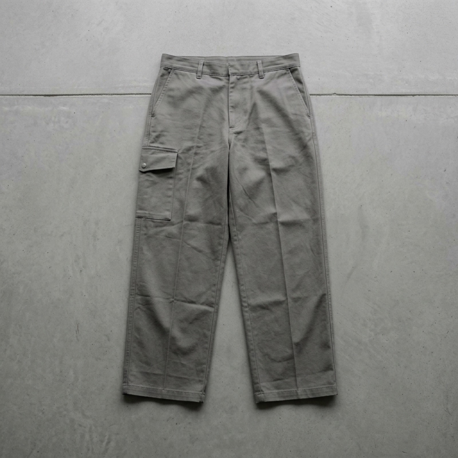 Wide ash-grey cotton trousers laid flat on concrete, shot from above.