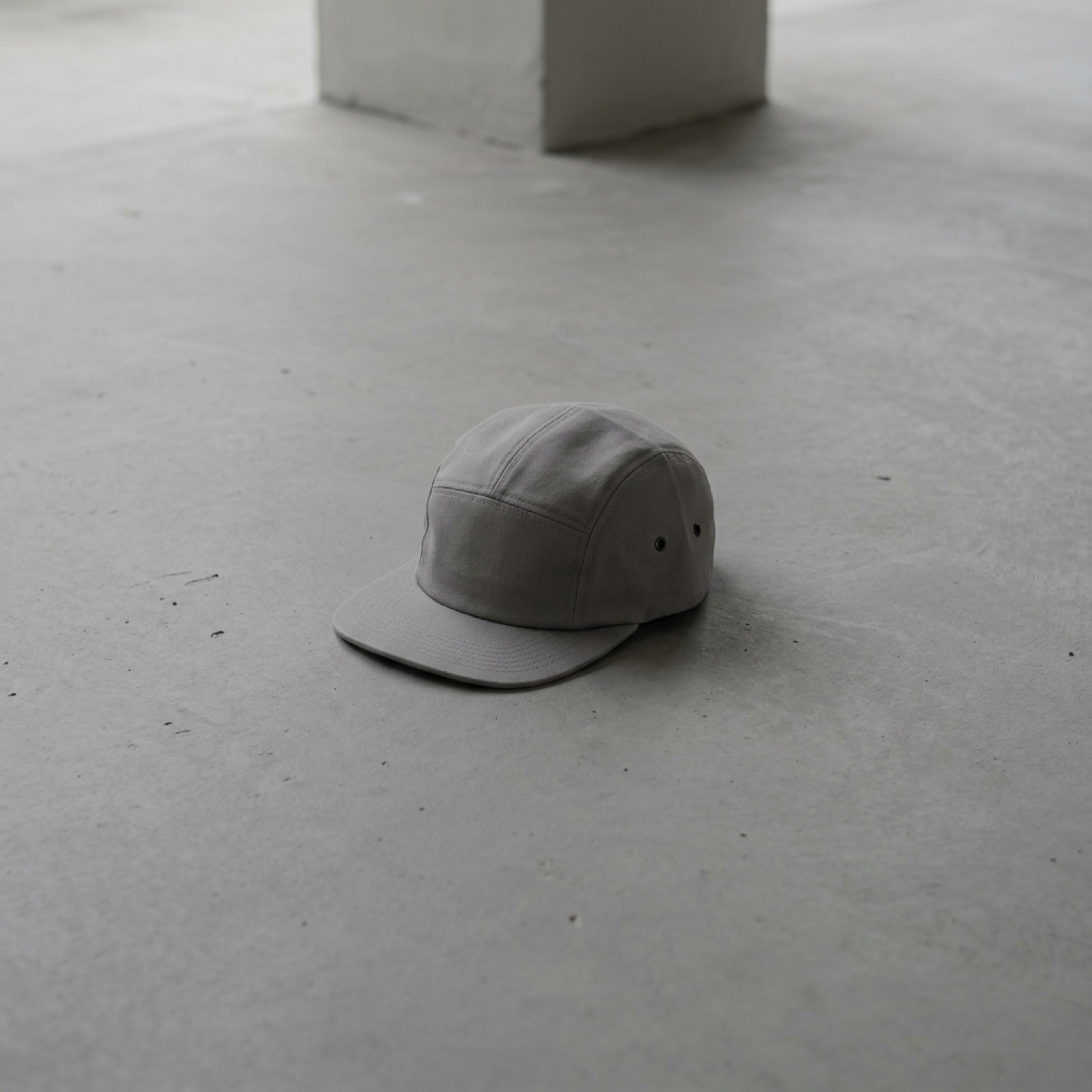 A grey five-panel cap alone on a wide expanse of concrete floor.