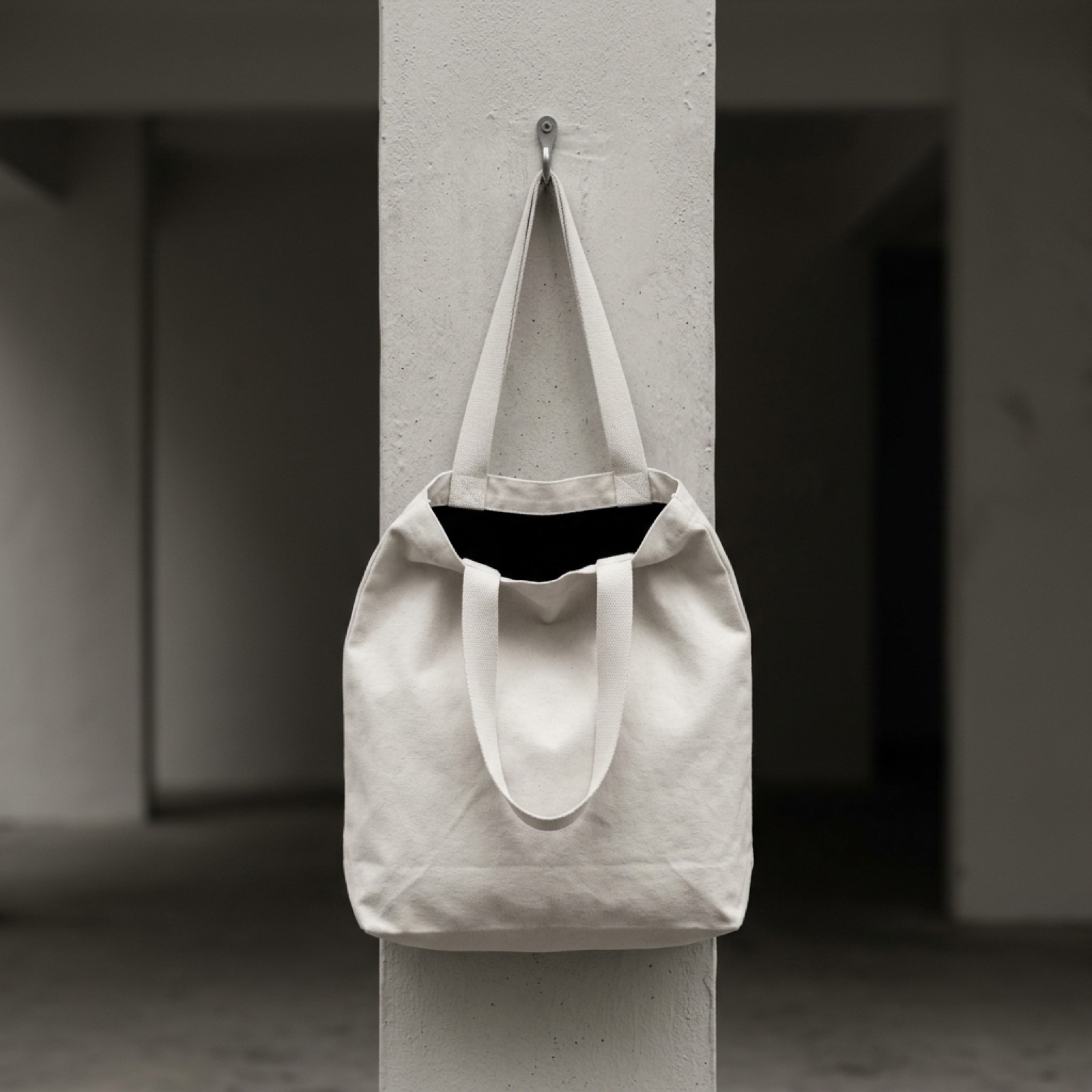 A bone canvas tote hanging from a steel hook on a pillar.
