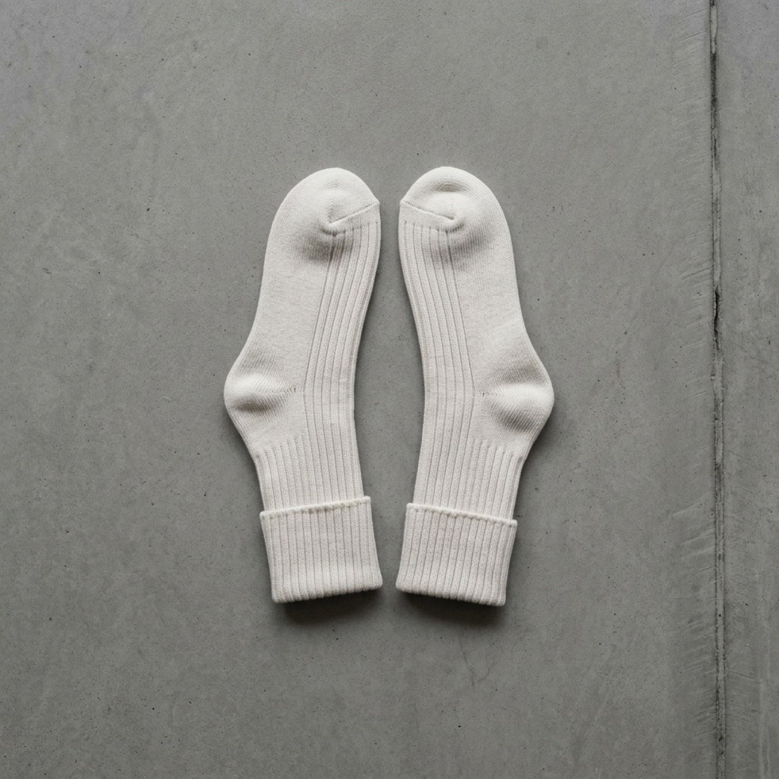 A pair of thick ribbed bone socks laid flat on concrete.